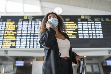 Woman wearing protective face mask talking on smart phone at airport - SNF00606