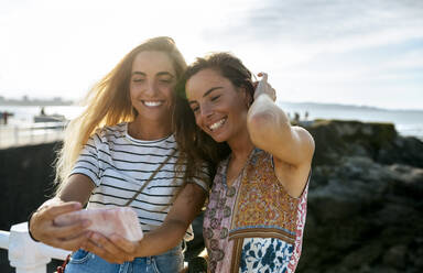 Lächelnde junge Schwestern machen am Wochenende ein Selfie am Strand - MGOF04481