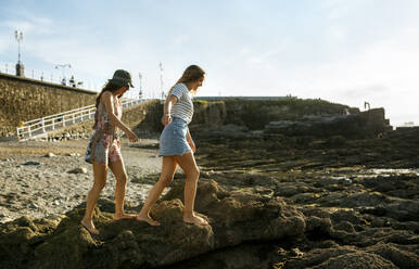 Junge Frauen gehen auf Felsen am Strand gegen den Himmel - MGOF04486