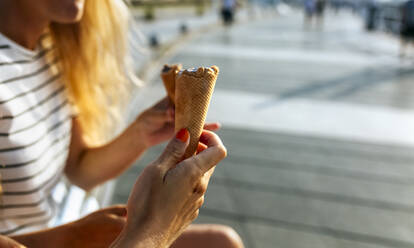 Junge Frauen essen Eis, während sie an einem sonnigen Tag ihre Freizeit in der Stadt verbringen - MGOF04492