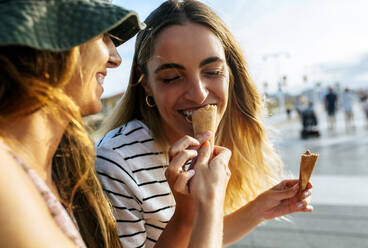 Smiling young woman feeding ice cream to sister while spending enjoying in city - MGOF04493