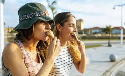 Young women looking away while eating ice cream in city during weekend - MGOF04494