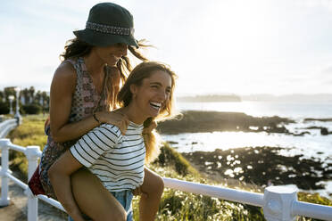 Carefree young woman piggybacking sister while enjoying weekend at beach on sunny day - MGOF04504