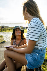 Lächelnde junge Frauen, die sich unterhalten, während sie ein Wochenende zusammen verbringen - MGOF04508