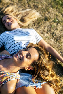 Fröhliche junge Frauen entspannen sich an einem sonnigen Tag auf einem Feld - MGOF04510
