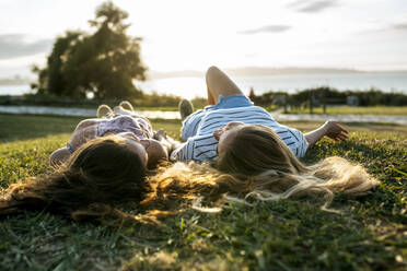 Young female friends relaxing on field while spending weekend together - MGOF04518