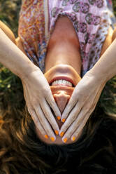 Smiling young woman covering eyes with hands while lying on field - MGOF04520