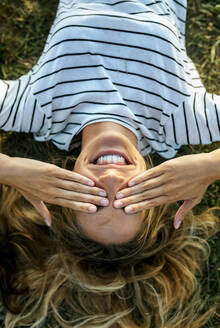 Glückliche junge Frau, die ihre Augen mit den Händen bedeckt, während sie sich auf einem Feld entspannt - MGOF04521