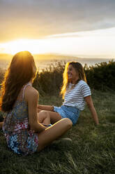 Lächelnde junge Frau verbringt ihre Freizeit mit einem Freund auf einem Feld bei Sonnenuntergang - MGOF04530