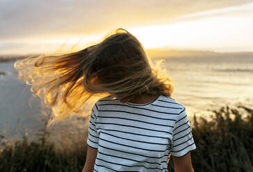 Junge Frau wirft ihr Haar gegen den bewölkten Himmel bei Sonnenuntergang - MGOF04532