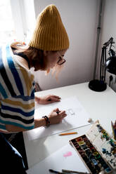 Side view of female artist in fancy wear sitting at table in studio and browsing mobile phone during work - ADSF16166