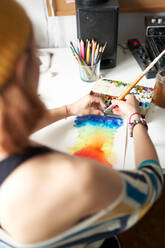 Rückenansicht einer anonymen Malerin, die in einer Werkstatt ein Aquarellbild mit Farbspektrum erstellt - ADSF16171
