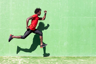 Side view of black sportsman in activewear in moment of jumping during intense workout on sunny day - ADSF16182