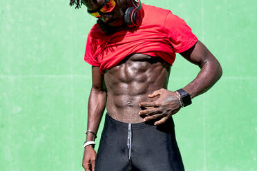 Crop African American male athlete demonstrating strong naked torso during training on sunny day on sports ground - ADSF16184