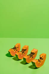 Von oben geschnittene Stücke frischer reifer süßer Papayafrüchte in einer Reihe auf hellgrünem Hintergrund angeordnet - ADSF16190