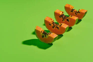 Von oben geschnittene Stücke frischer reifer süßer Papayafrüchte in einer Reihe auf hellgrünem Hintergrund angeordnet - ADSF16191