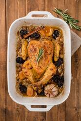 Top view of stuffed baked chicken in dish with garlic and cinnamon stick placed on wooden table - ADSF16196