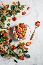 Top view of nutritious smoothie bowl with strawberries and nuts arranged on table with green plant and various fruits - ADSF16237