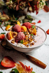 Top view of nutritious smoothie bowl with strawberries and nuts arranged on table with green plant and various fruits - ADSF16239