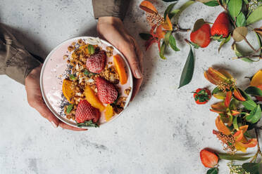 Von oben von einer nicht erkennbaren Frau mit einer Smoothie-Schale mit Früchten und Beeren am Tisch sitzend beim Frühstück am Morgen - ADSF16240