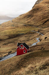 Enge Landstraße und kleines Häuschen an der Küste des ruhigen Meeres an einem bewölkten Tag auf den Färöer Inseln - ADSF16250