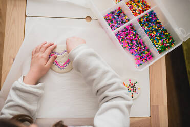 Von oben auf ein nicht erkennbares Kind, das mit bunten Mosaiksteinen spielt, während es zu Hause Spaß hat - ADSF16277