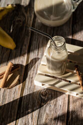 Von oben Glasgefäß mit gesundem Bananen-Zimt-Milchshake, serviert auf Holztisch mit Zutaten - ADSF16303