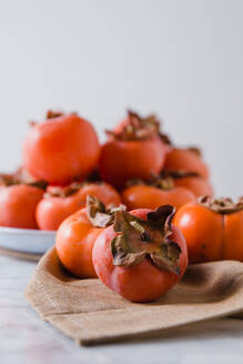 Fresh persimmons on plate placed on white table in bright kitchen - ADSF16314