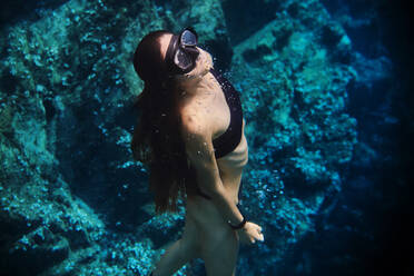 Young female diver in swimsuit and snorkeling mask floating in clean transparent sea water - ADSF16352