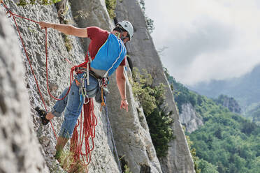 Rückenansicht eines nicht erkennbaren männlichen Bergsteigers in Sicherheitsausrüstung beim Klettern in steilem Fels während des Sommerurlaubs - ADSF16354