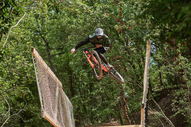 Low angle of brave male in helmet performing extreme trick on bicycle for downhill in woods - ADSF16356