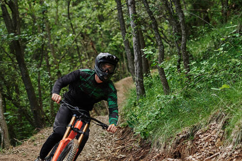 Männlicher Radfahrer auf dem Fahrrad, der bergab auf einem sandigen Weg fährt und einen extremen Trick im Wald ausführt - ADSF16357