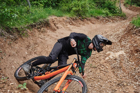 Männlicher Radfahrer auf dem Fahrrad, der bergab auf einem sandigen Weg fährt und einen extremen Trick im Wald ausführt - ADSF16358