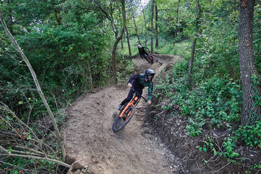 Male cyclist on bike for downhill riding along sandy path and performing extreme trick in woods - ADSF16359