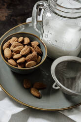 From above ceramic bowl with fresh almonds placed on plate near bottle of vegan milk and strainer - ADSF16393