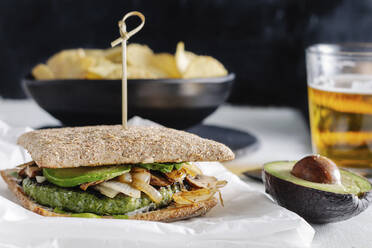 Leckeres Sandwich mit Avocado auf dem Tisch mit einem Glas Bier und Kartoffelchips im Café - ADSF16411