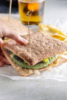 Unbekannte Person mit schmackhaftem Sandwich mit Gemüseschnitzel auf einem Tisch mit einem Glas Bier in einem Cafe - ADSF16415