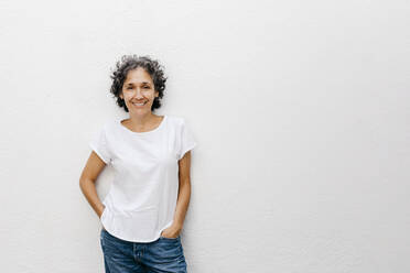 Smiling mature woman with short hair standing against white wall - TCEF01202
