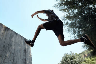 Low angle side view of unrecognizable strong male doing parkour and jumping above ground while performing dangerous trick - ADSF16422