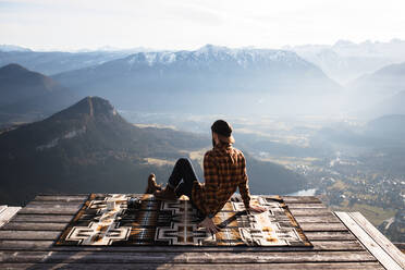 Rückenansicht eines nicht erkennbaren männlichen Touristen, der an einem Aussichtspunkt auf einer Decke sitzt und die morgendliche Landschaft des Bergkamms genießt - ADSF16429