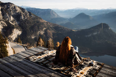 Rückenansicht eines nicht erkennbaren weiblichen Touristen, der an einem Aussichtspunkt in den Bergen sitzt und die herrliche Landschaft am Morgen beobachtet - ADSF16431