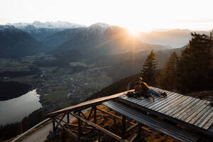 Rückenansicht eines nicht erkennbaren Paares von Reisenden, die auf einer Holzterrasse liegen und den Sonnenaufgang im Hochland am nebligen Morgen genießen - ADSF16434