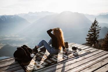 Seitenansicht eines nicht erkennbaren weiblichen Touristen, der an einem Aussichtspunkt in den Bergen sitzt und die herrliche Landschaft am Morgen beobachtet - ADSF16435