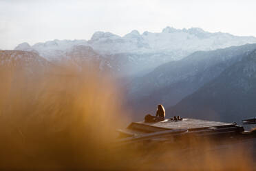 Seitenansicht eines nicht erkennbaren weiblichen Touristen, der an einem Aussichtspunkt in den Bergen sitzt und die herrliche Landschaft am Morgen beobachtet - ADSF16436