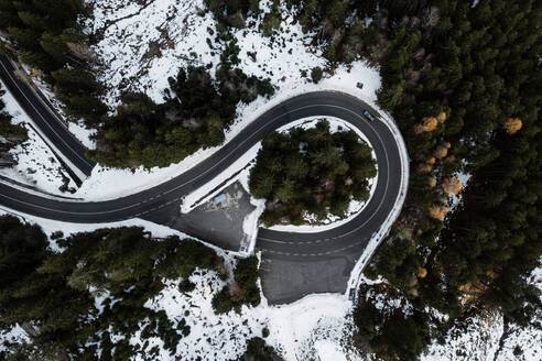 Spektakuläre Drohnenansicht eines einsamen Autos an einer Straßenkreuzung in einem Nadelwald mit Schnee im Winter - ADSF16441