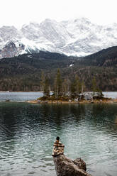 Rückenansicht eines nicht erkennbaren Touristen, der auf einem Stein am Ufer eines Teiches sitzt und die im Winter verschneiten Berge betrachtet - ADSF16446