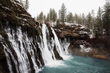 Malerische Landschaft der mächtigen Wasserfall mit Pool fließt unter verschneiten Wald in bergigem Gelände im Winter Tag in den USA - ADSF16452