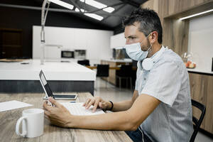 Businessman wearing protective mask while using laptop at desk in office during COVID-19 pandemic - RCPF00293