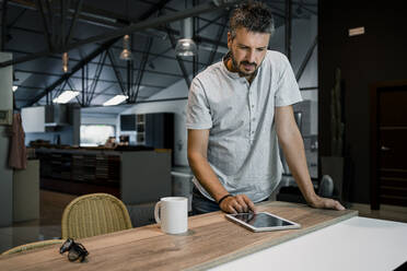 Männlicher Fachmann, der ein digitales Tablet benutzt, während er freiberufliche Arbeit am Schreibtisch im Büro verrichtet - RCPF00302