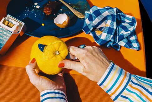 Hands of senior woman peeling orange with table knife - ERRF04555